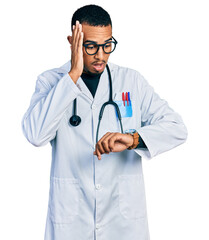Fototapeta premium Young african american man wearing doctor uniform and stethoscope looking at the watch time worried, afraid of getting late
