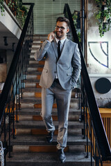 Obraz premium Handsome and smiled middle age businessman using his smart phone while standing in modern office or cafe bar.