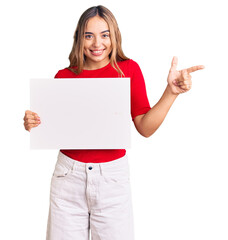 Young beautiful blonde woman holding blank empty banner smiling happy pointing with hand and finger to the side