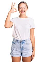 Fototapeta premium Young beautiful blonde woman wearing casual white tshirt smiling positive doing ok sign with hand and fingers. successful expression.
