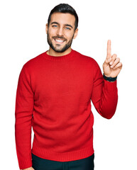Fototapeta premium Young hispanic man wearing casual clothes showing and pointing up with finger number one while smiling confident and happy.