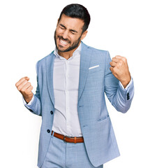 Young hispanic man wearing business jacket very happy and excited doing winner gesture with arms...