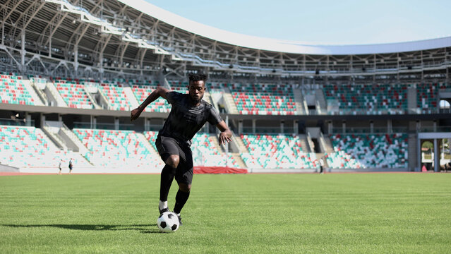 African American man playing football on the stadium field. A man runs with a soccer ball across the field.