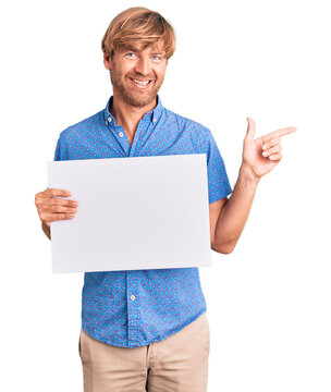 Handsome caucasian man with beard holding sale poster smiling happy pointing with hand and finger to the side