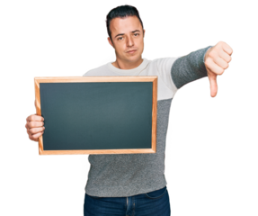 Handsome young man holding blackboard with angry face, negative sign showing dislike with thumbs down, rejection concept