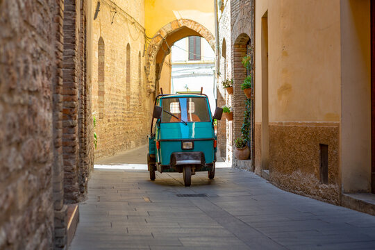 Man in a azul blue tricycle driving in the narrow streets of old italian town of Spello in Perugia.