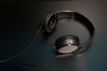 black headphones with a wire lying on a black reflective surface