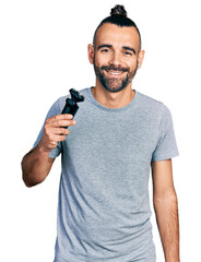 Hispanic man with ponytail holding electric razor machine looking positive and happy standing and...