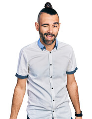 Hispanic man with ponytail wearing casual white shirt winking looking at the camera with sexy expression, cheerful and happy face.