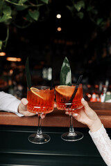 hands of woman and man are clinking, cheers with glasses of Spritz cocktail. Couple celebrating...