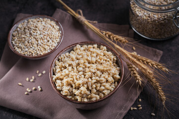 Bowl of cooked peeled barley grains porridge with ears of wheat on dark wooden background. Cooking Healthy and diet food concept