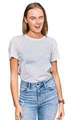 Obraz premium Beautiful young blonde woman wearing casual white t shirt winking looking at the camera with sexy expression, cheerful and happy face.