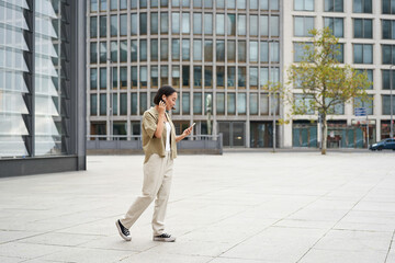 Fototapeta na wymiar Silhouette of asian woman walking on street in wireless headphones, holding smartphone