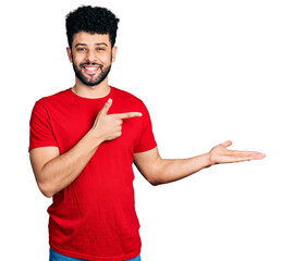 Young arab man with beard wearing casual red t shirt amazed and smiling to the camera while presenting with hand and pointing with finger.