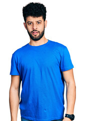 Fototapeta premium Young arab man with beard wearing casual blue t shirt in shock face, looking skeptical and sarcastic, surprised with open mouth