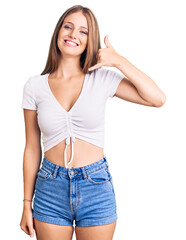 Fototapeta premium Young beautiful blonde woman wearing casual white tshirt smiling doing phone gesture with hand and fingers like talking on the telephone. communicating concepts.
