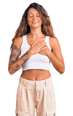 Young hispanic woman with tattoo wearing casual clothes smiling with hands on chest with closed eyes and grateful gesture on face. health concept.