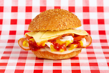 Hamburger with ham, lettuce, tomato, onion, mayonnaise and mustard on the background of a checkered red and white tablecloth.