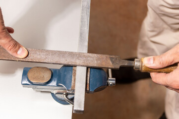 Man works with iron pipe or metallic aluminum file rasp gripped in vise on workbench table in...