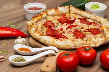 Tasty pizza with pepperoni, ham and peppers and pizza ingredients around the table