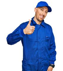 Bald man with beard wearing builder jumpsuit uniform doing happy thumbs up gesture with hand....