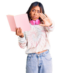 Naklejka premium Young beautiful mixed race woman reading a book wearing headphones with open hand doing stop sign with serious and confident expression, defense gesture