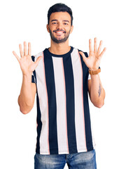 Young handsome hispanic man wearing striped tshirt showing and pointing up with fingers number ten while smiling confident and happy.