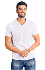 Young handsome hispanic man wearing casual clothes with hands together and crossed fingers smiling relaxed and cheerful. success and optimistic
