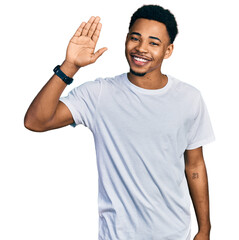 Young african american man wearing casual white t shirt waiving saying hello happy and smiling, friendly welcome gesture © Krakenimages.com