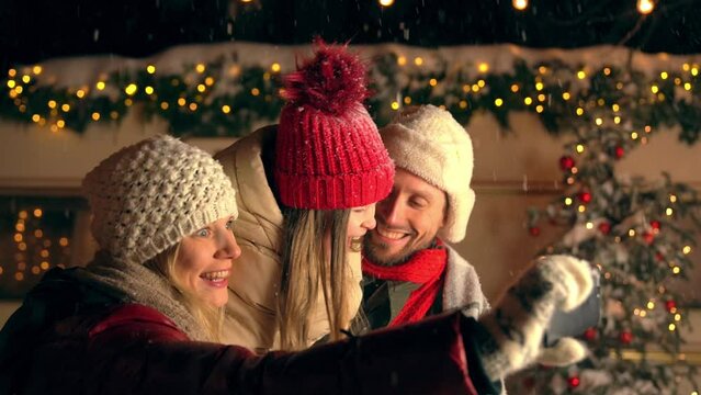 Happy young mother, father, child, daughter taking selfie with cosy house, van home behind at snowing weather. Near big green Christmas tree, waiting for present. New Year eve, winter holiday concept.