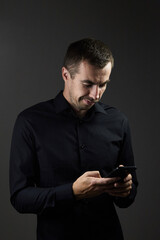 Young man using phone with smile on dark background