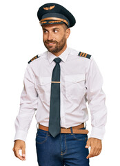Handsome man with beard wearing airplane pilot uniform looking away to side with smile on face, natural expression. laughing confident.