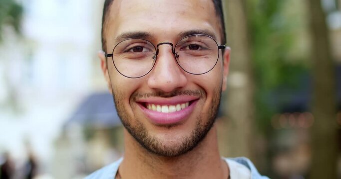 Close up of smiling cheerful young male face in eyeglasses. Portrait of happy joyful handsome man in glasses at street. Outdoors. Happiness emotions and expressing joy concept.