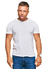 Fototapeta premium Handsome muscle man wearing casual white tshirt sticking tongue out happy with funny expression. emotion concept.