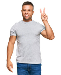 Naklejka premium Handsome muscle man wearing casual grey tshirt smiling with happy face winking at the camera doing victory sign. number two.