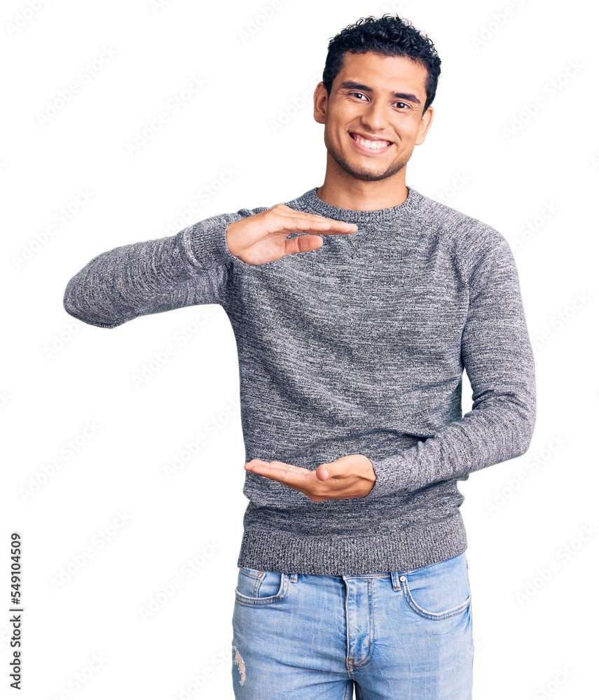 Sticker Hispanic handsome young man wearing casual sweater gesturing with hands showing big and large size sign, measure symbol. smiling looking at the camera. measuring concept.