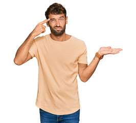 Handsome young man with beard wearing casual tshirt confused and annoyed with open palm showing copy space and pointing finger to forehead. think about it.
