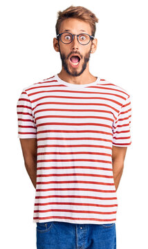 Handsome blond man with beard wearing casual clothes and glasses afraid and shocked with surprise and amazed expression, fear and excited face.