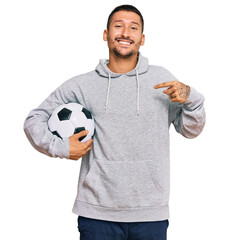 Handsome man with tattoos holding soccer ball pointing finger to one self smiling happy and proud