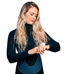 Young blonde woman wearing diver neoprene uniform checking the time on wrist watch, relaxed and...
