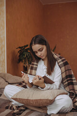Obraz premium Calm focused woman in warm plaid sitting on bed and reading book while relaxing at home 