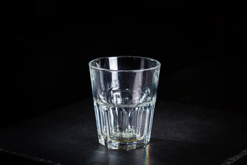 Faceted empty glass stands on a black slate plate.