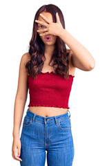 Fototapeta premium Young beautiful chinese girl wearing casual clothes peeking in shock covering face and eyes with hand, looking through fingers with embarrassed expression.