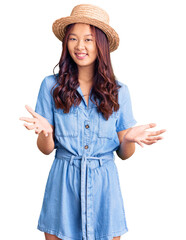 Young beautiful chinese girl wearing summer hat smiling cheerful with open arms as friendly welcome, positive and confident greetings