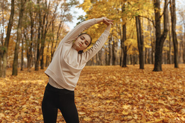Confident female runner exercising in park during training and stretching while doing side bend and looking at camera 