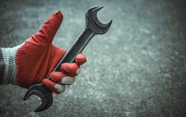 A man's gloved hand holds a large iron wrench for unscrewing nuts. Thumbs up in a glove. Master...