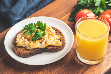 Scrambled eggs with parsley on bread at white plate, homemade healthy breakfast on wooden board
