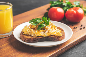 Scrambled eggs with parsley on bread at white plate, homemade healthy breakfast on wooden board