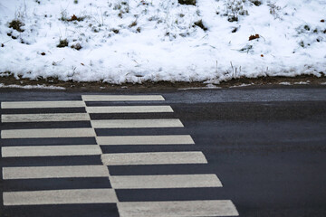 Road crossing zebra on black wet asphalt road with snow covered sides low angle view