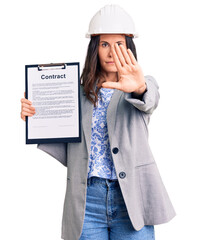 Young beautiful brunette woman wearing architect hardhat holding contract with open hand doing stop sign with serious and confident expression, defense gesture